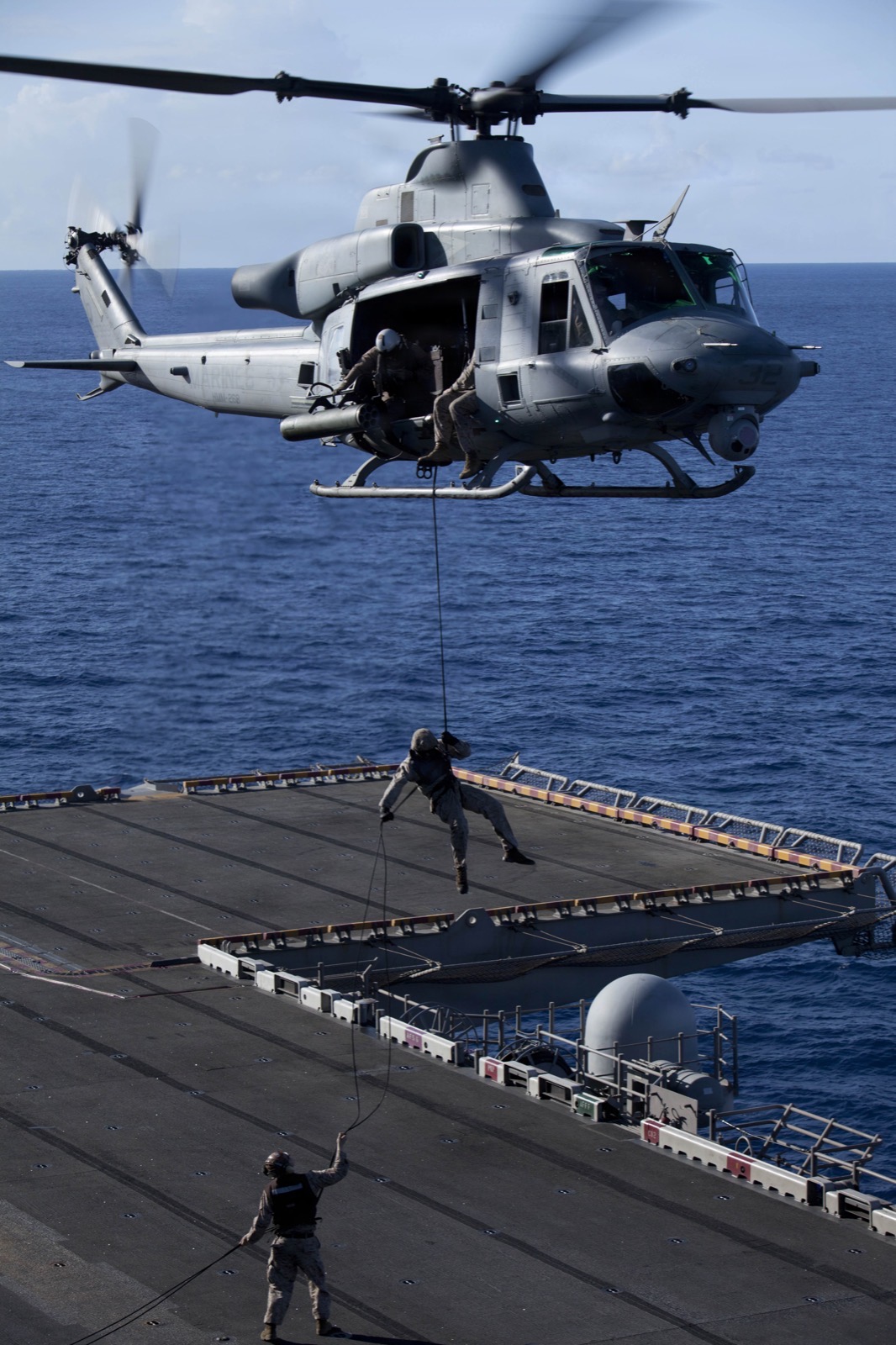 A service member fast-roping from a hovering helicopter onto a ship deck