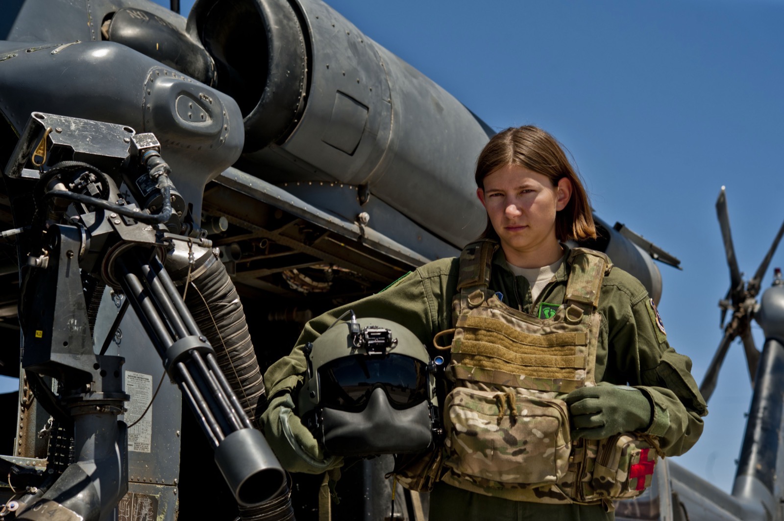 An airman beside a mounted gun on an aircraft, gear in hand
